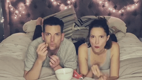 GIF of white hetero couple smiling and cheerfully watching TV